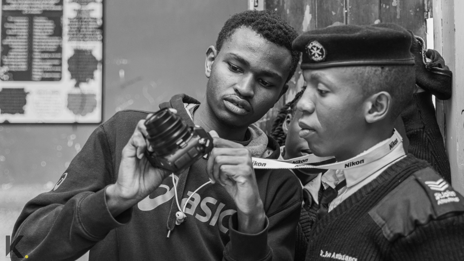 Two young men examining a camera lens together.